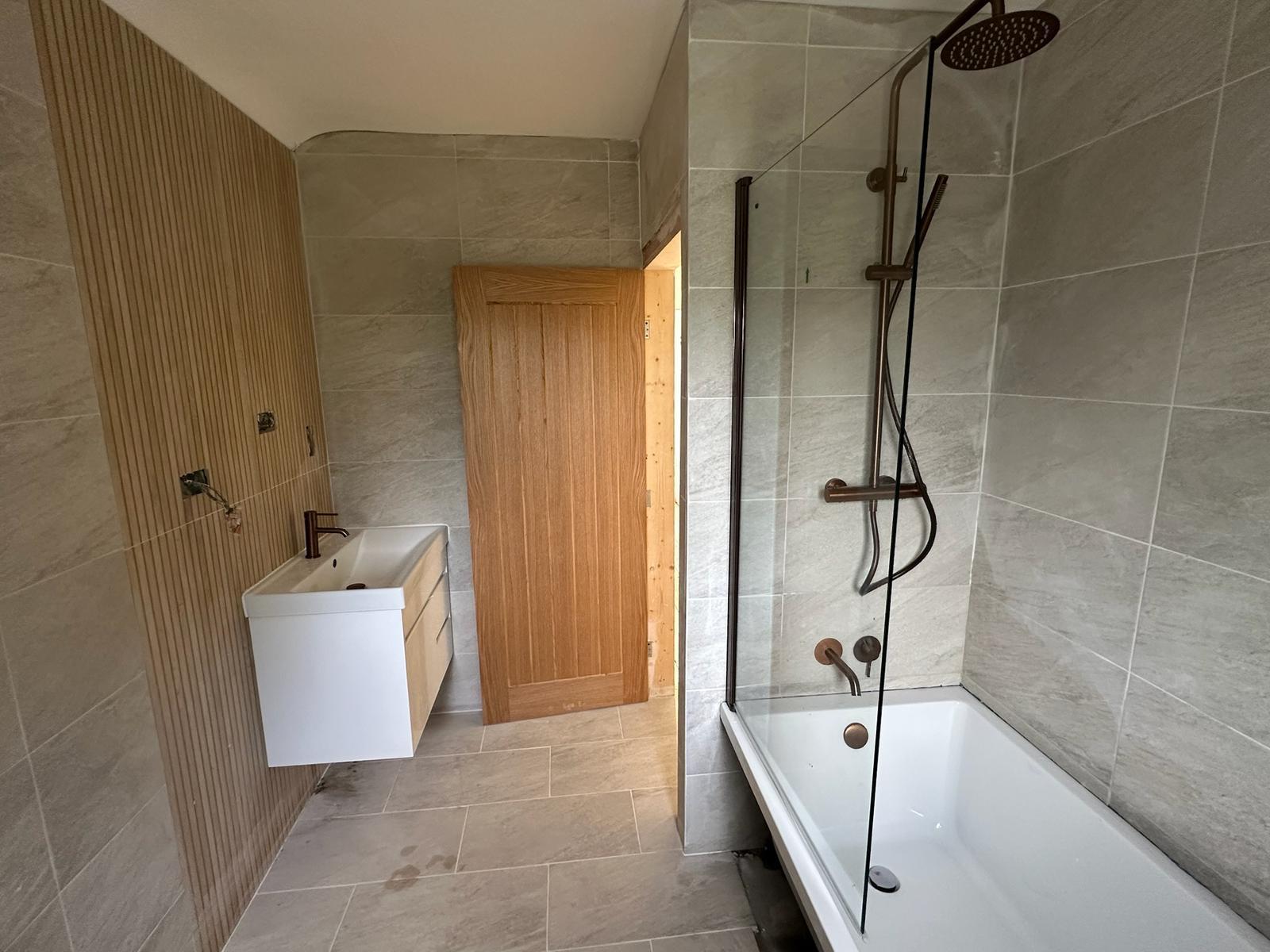 Bathroom installation with stone tiles, bath and black shower fittings